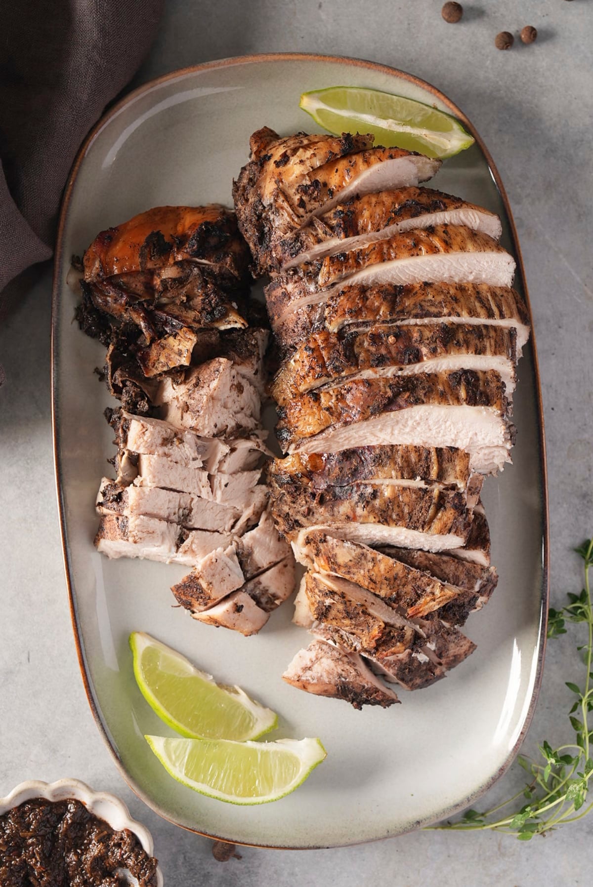 Jerk turkey breast carved into slices on a white platter with lime wedges, showing white meat under a dark seasoned crust.