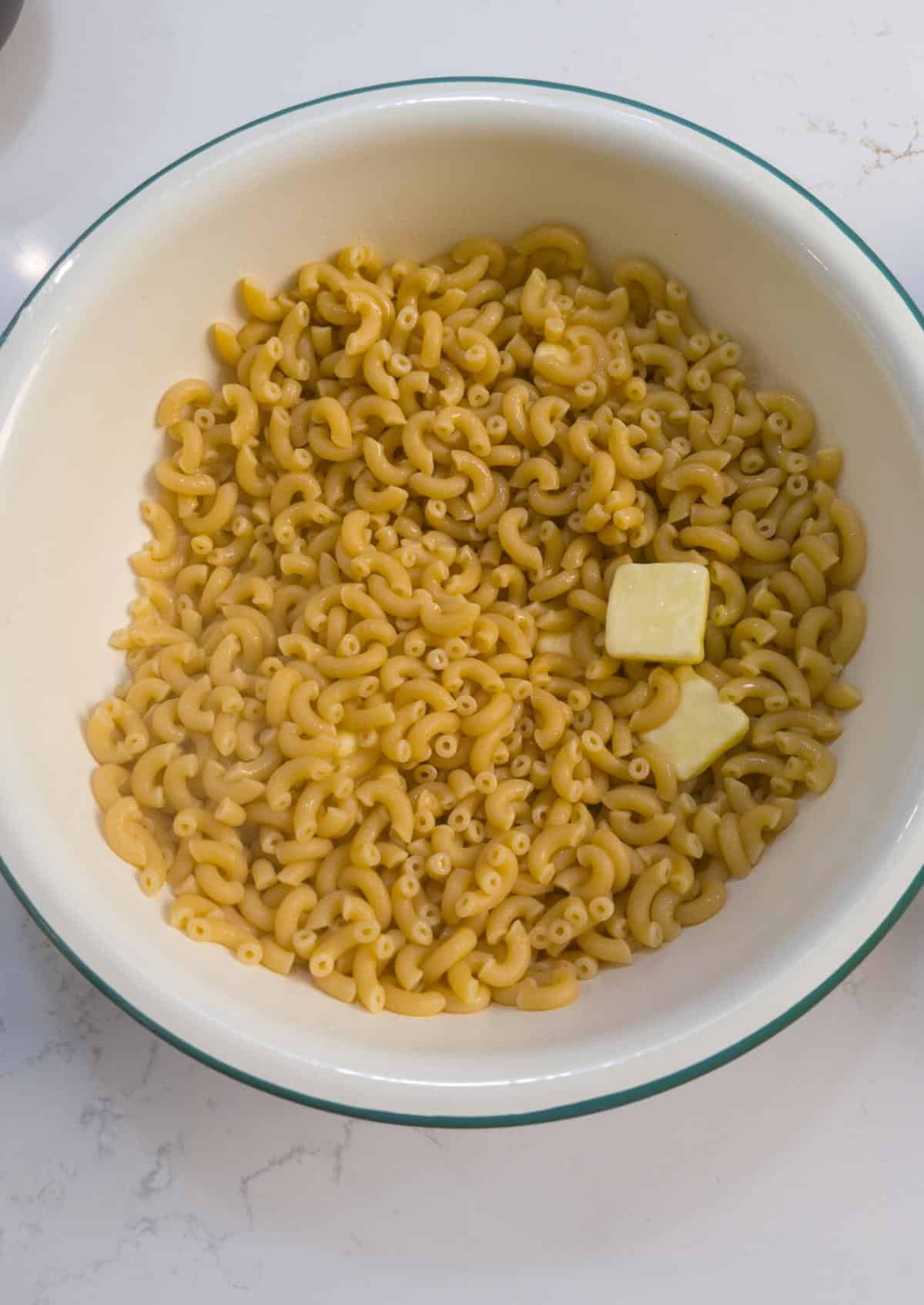 Butter melting on hot elbow macaroni in a large white bowl.