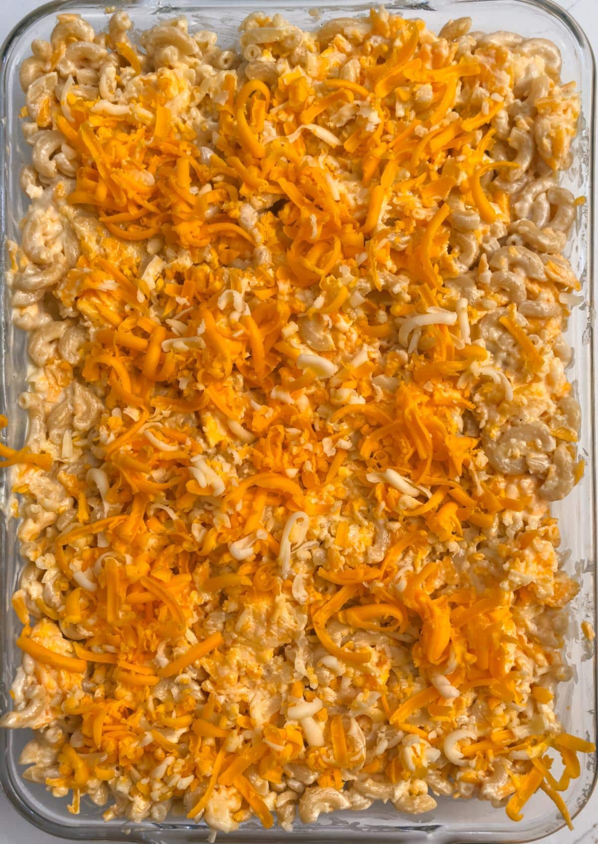Unbaked macaroni spread in a glass baking dish and covered with the reserved shredded cheese.