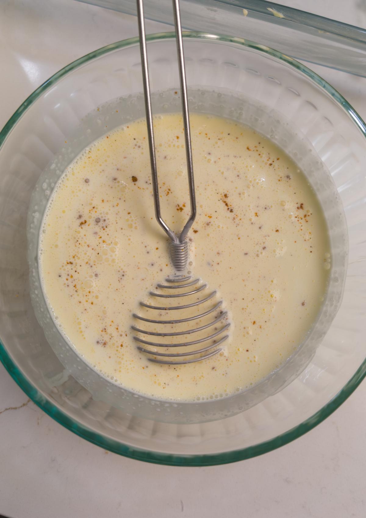 The egg and cream mixture whisked smooth in a glass bowl, flecked with seasoning.