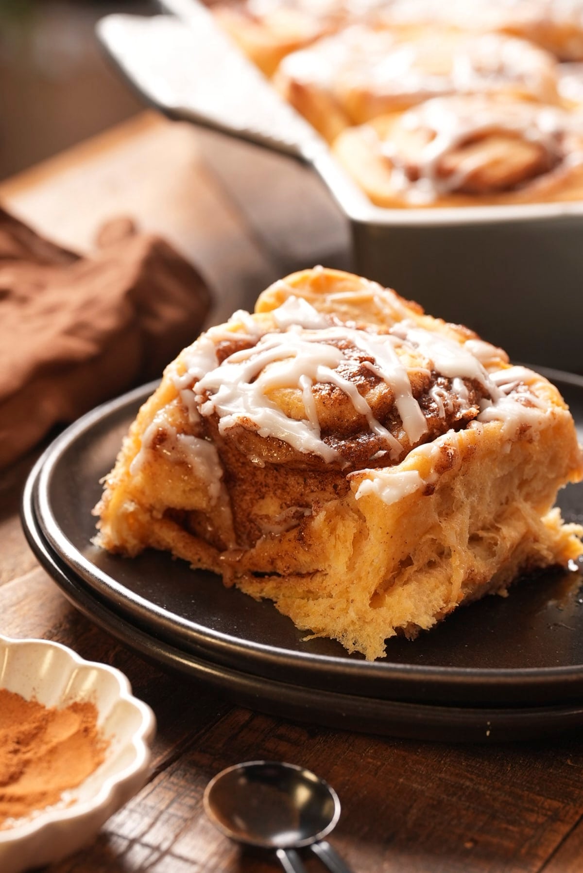 A single glazed sweet potato cinnamon roll on a dark plate.