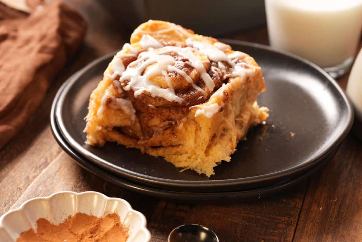 A glazed sweet potato cinnamon roll on a plate next to a glass of milk.