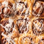 Close-up of glazed rolls in the pan, with maple glaze running into the swirls.