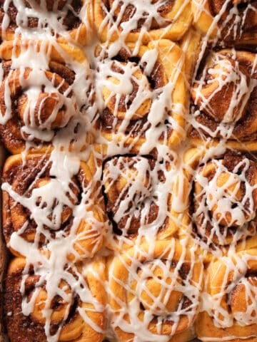 Close-up of glazed rolls in the pan, with maple glaze running into the swirls.