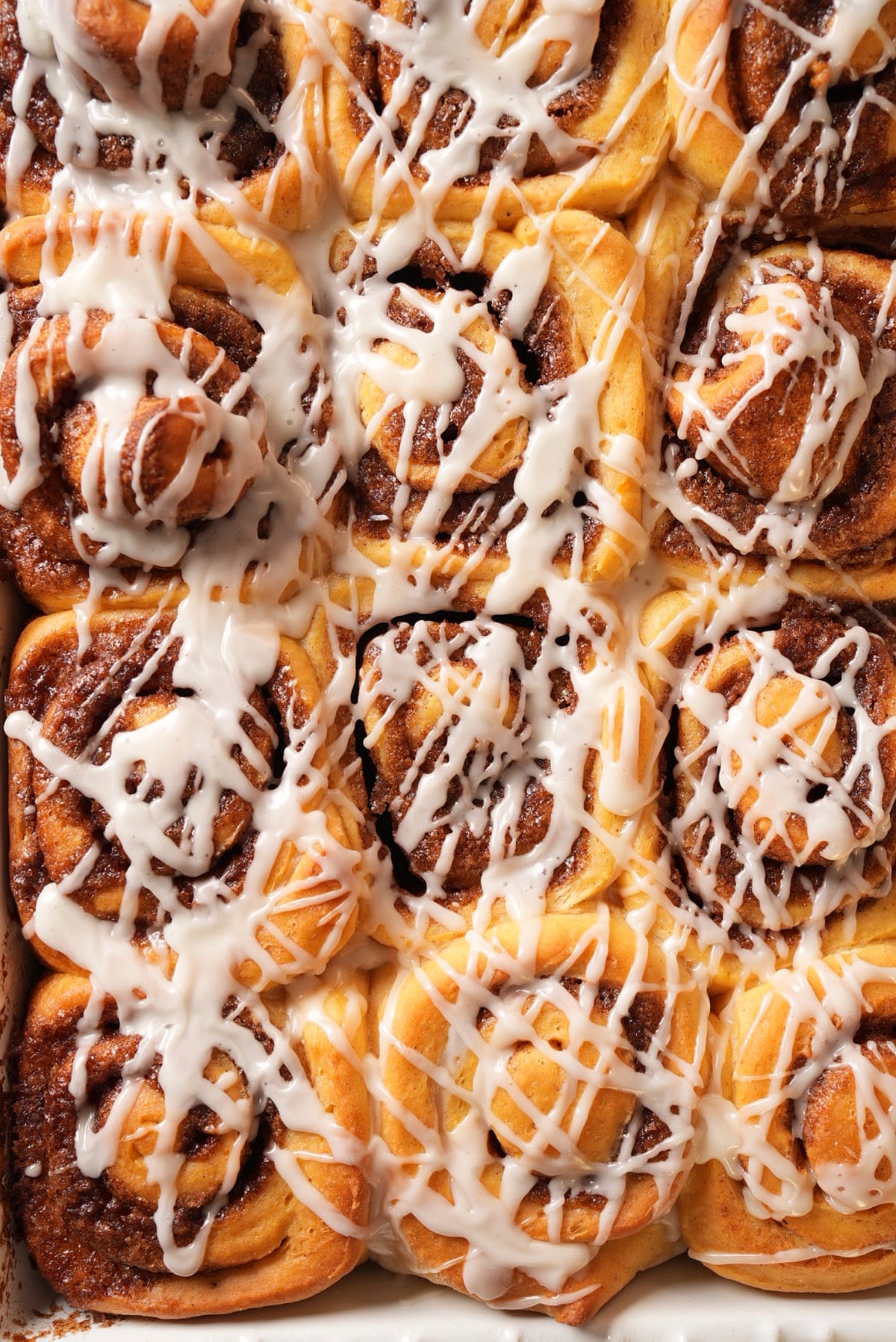 Close-up of glazed rolls in the pan, with maple glaze running into the swirls.